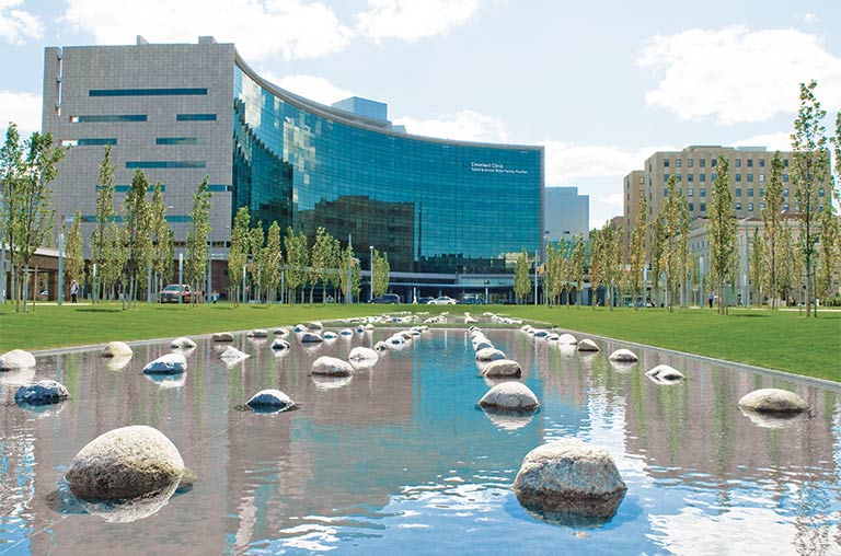 Cleveland Clinic building at the end of a shallow pond with rocks.